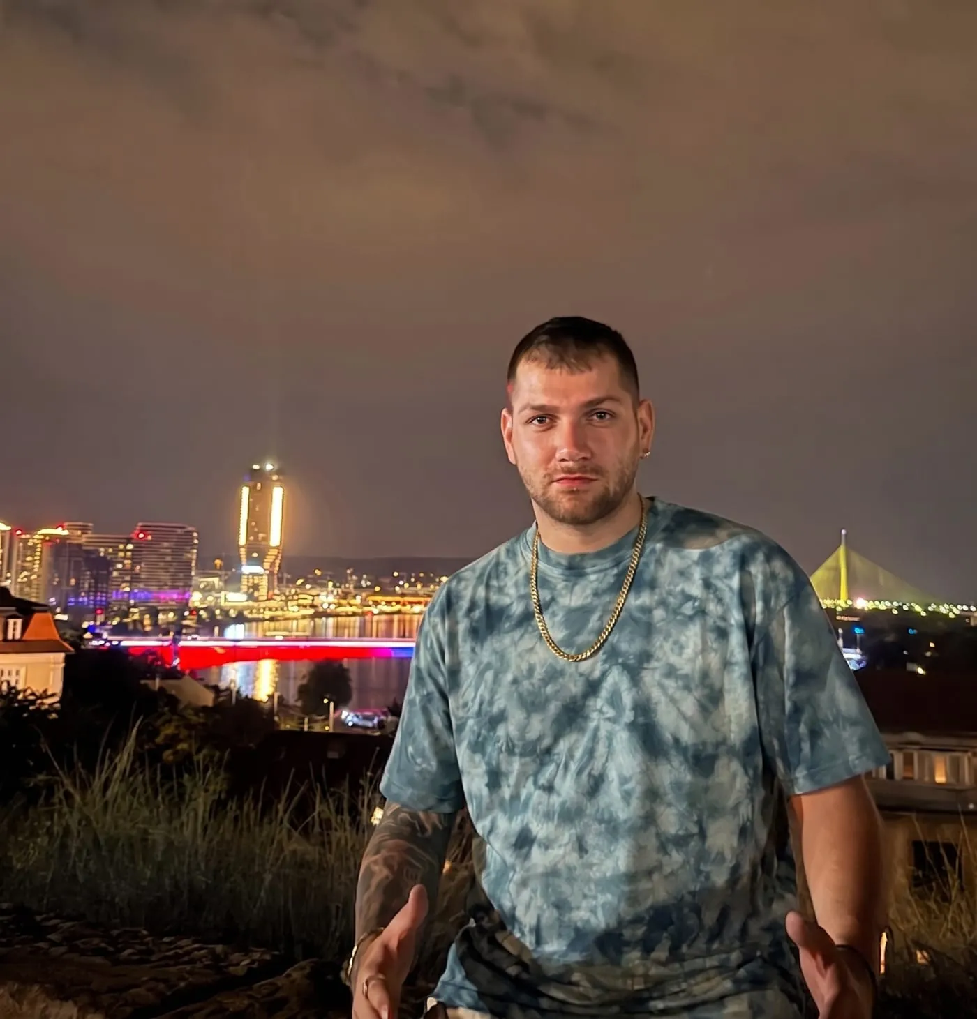 An ice-dyed tee worn above the Sava at night, the lights of Novi Beograd and the bridges behind.