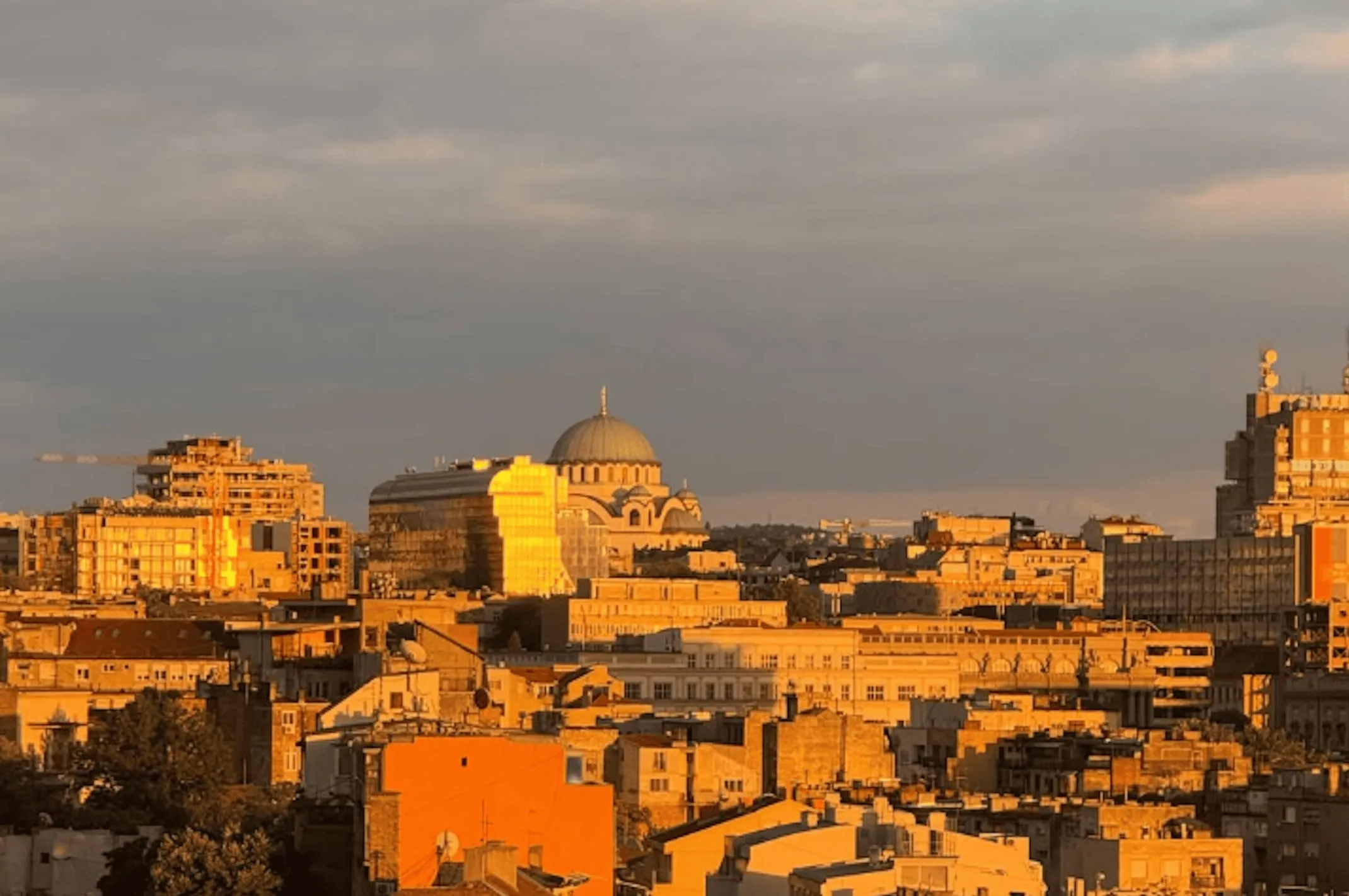 Belgrade rooftops at sunset, the dome of Saint Sava above them.